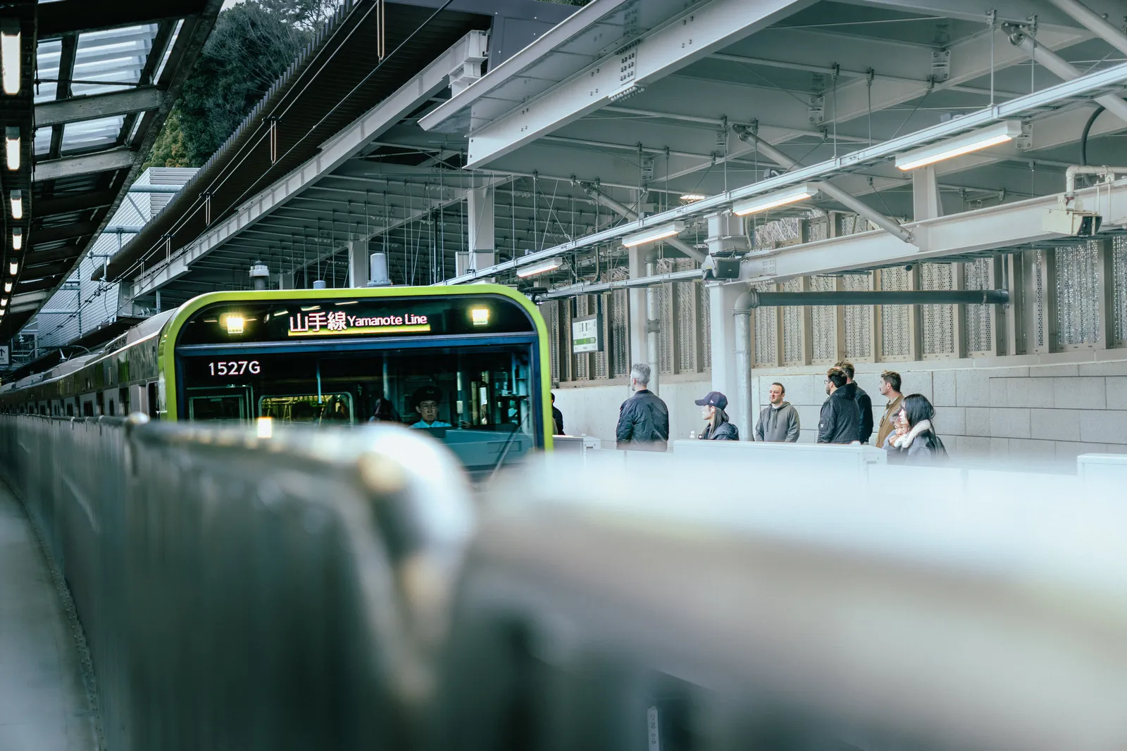 רכבת קו יאמאנוטה בתחנה בטוקיו, נוסעים ממתינים על הרציף באור יום