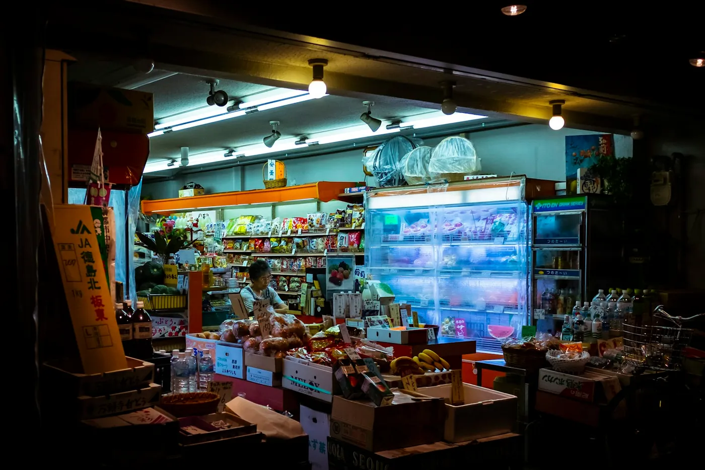 חנות מזון בשוק מקורה בקיוטו עם ארגזי מוצרים ותצוגה מוארת, יפן