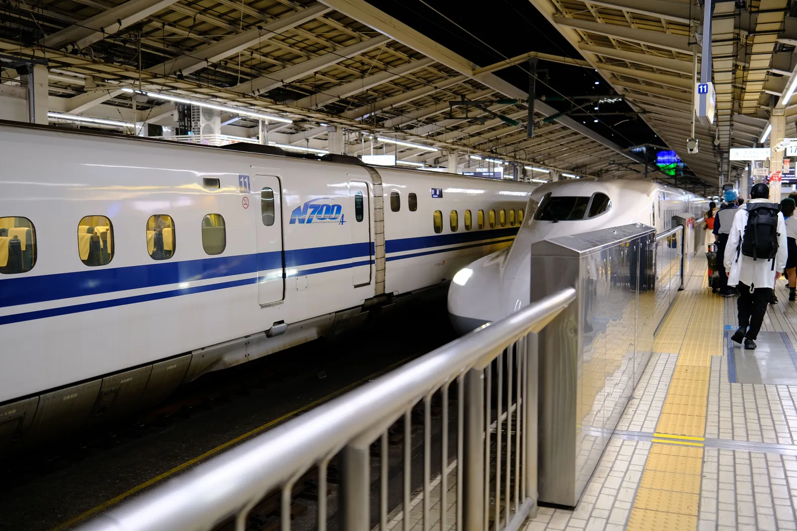 רכבת שינקנסן לבנה עומדת ברציף תחנה ביפן, נוסעים ממתינים