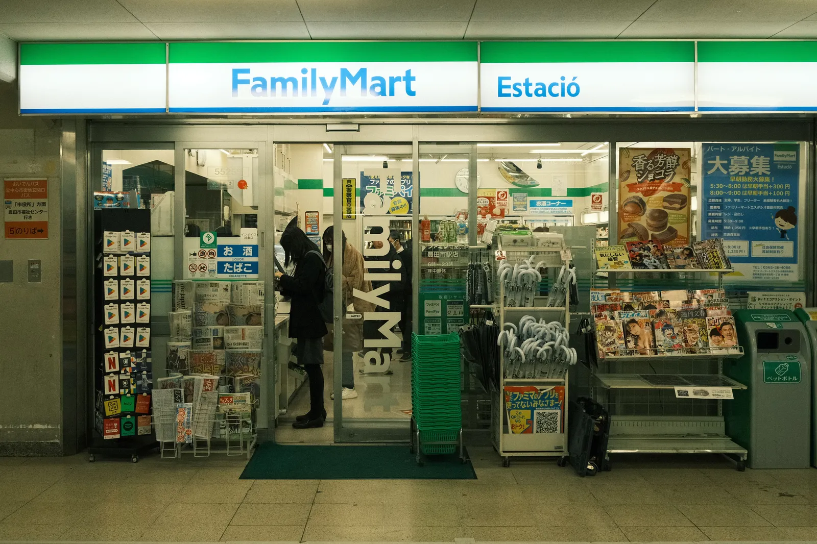 חזית חנות נוחות יפנית עם מדפי מגזינים בכניסה ולקוחות בפנים