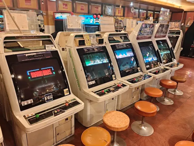 שורת מכונות משחקי ארקייד ישנות עם שרפרפים כתומים על רצפה אדמדמה