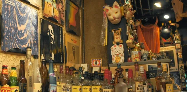 בקבוקי משקאות מול קיר מכוסה עטיפות תקליטים ופסלוני חתולים
