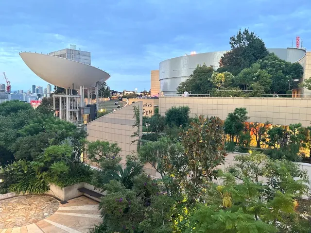 גג ירוק עם שיחים ושבילים, מבנים מעוגלים וקו רקיע בדמדומים