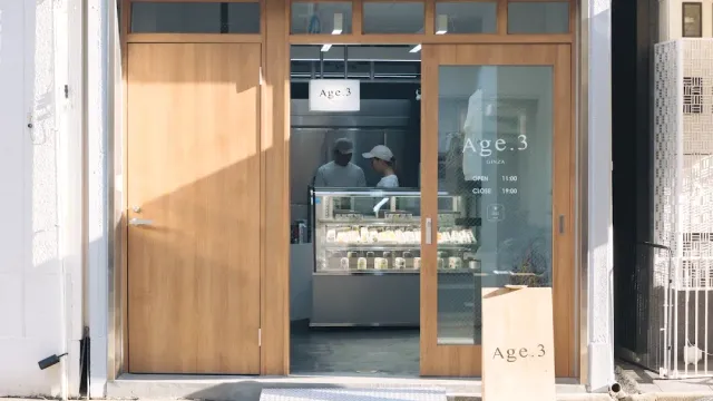 חזית עם דלתות עץ בהירות, ויטרינה מקוררת ושני עובדים מאחוריה