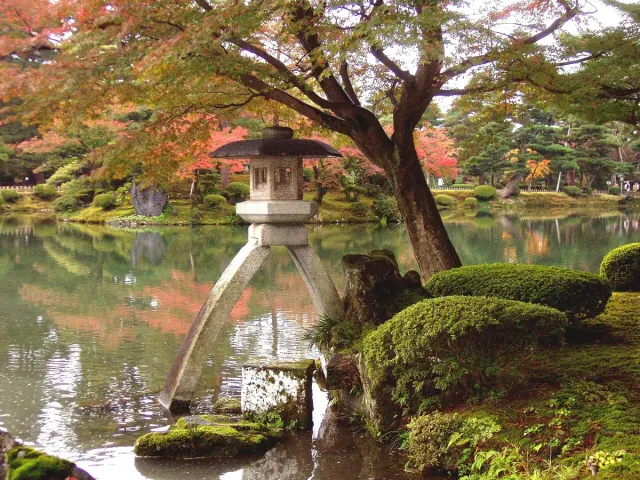 פנס אבן על רגליים דקות בשפת בריכה, בין עצים ואזוב
