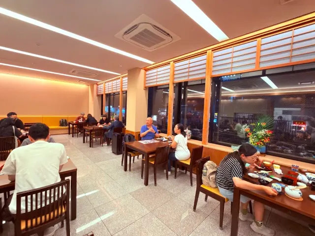 אולם אכילה מואר עם שולחנות עץ, סועדים וחלונות ארוכים לאורך הקיר