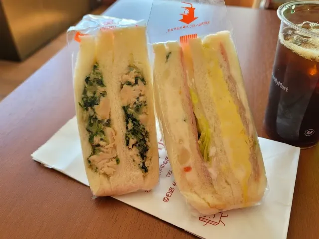 שני כריכים ארוזים בניילון, אחד עם עוף וירק ואחד עם ביצה, לצד כוס קרה