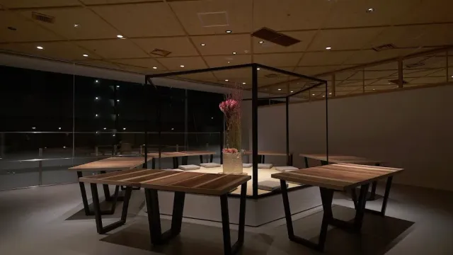 חדר אפלולי עם שולחנות עץ סביב מסגרת מתכת שחורה ובתוכה סידור פרחים