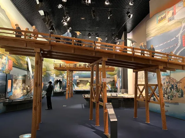 גשר עץ בגודל מלא בתוך אולם תצוגה, עם דמויות ותצוגות מתחתיו