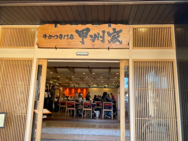 כניסת עץ עם שלט מגולף גדול, ודלתות פתוחות אל אולם מלא סועדים