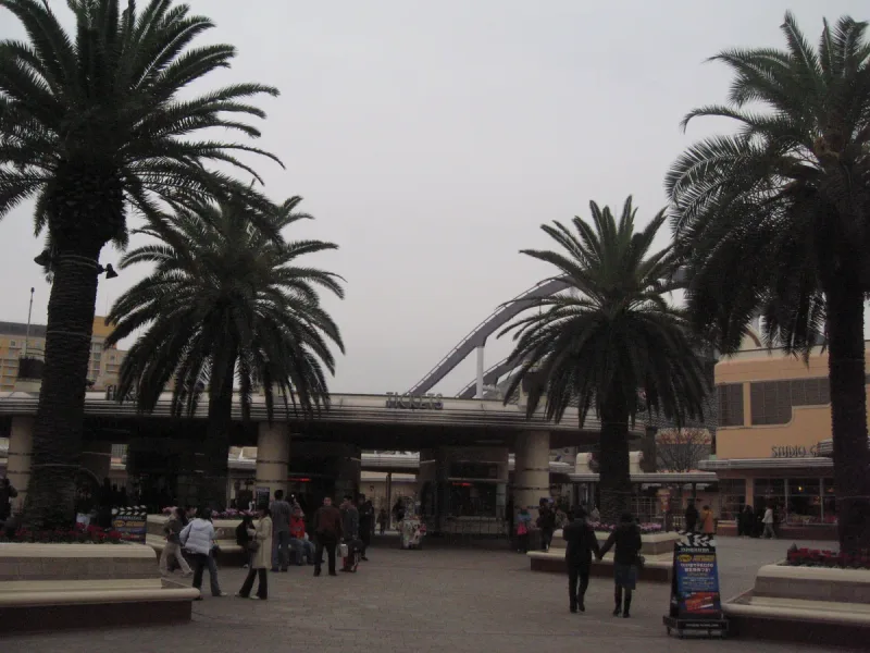 רחבת כניסה לפארק שעשועים עם שורת דקלים, שער וקהל מבקרים