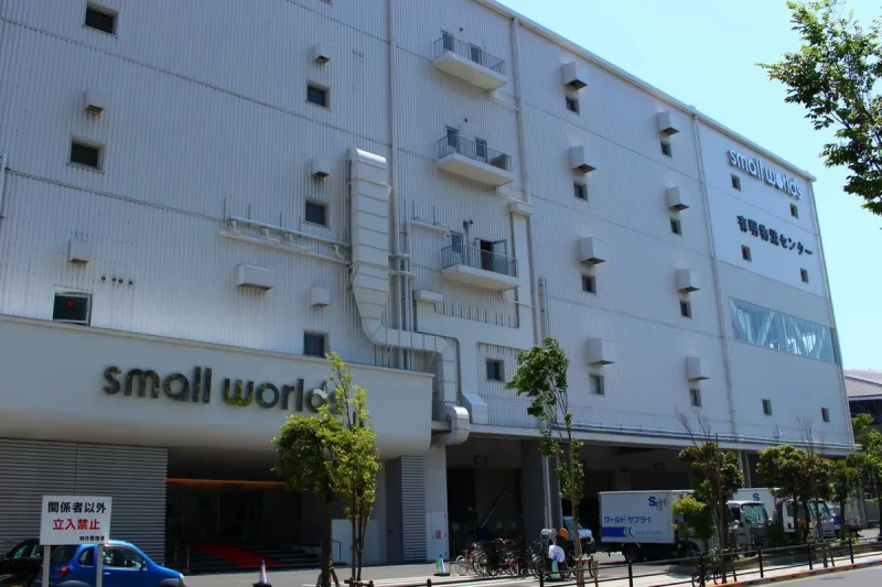 חזית בניין לבן עם שלט small worlds ורחוב עם עצים לפניו