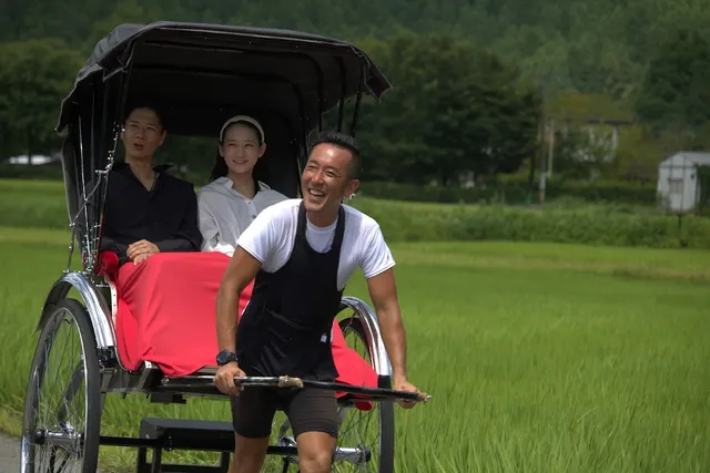 מושך ריקשה מחייך גורר זוג נוסעים לאורך שדות אורז ירוקים