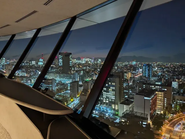 נוף עיר מוארת בלילה מבעד לחלונות משופעים של קומת תצפית