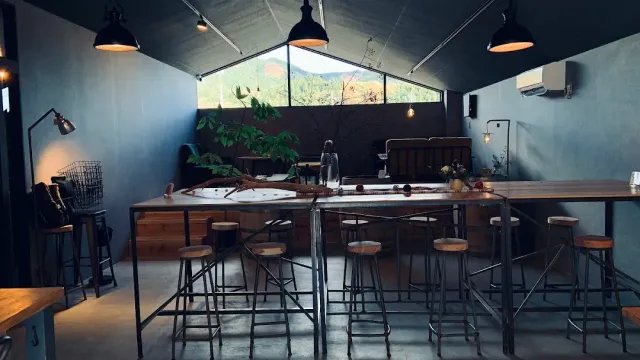 חלל עם שולחנות גבוהים ושרפרפים, מנורות תעשייתיות וחלון משולש אל גבעות