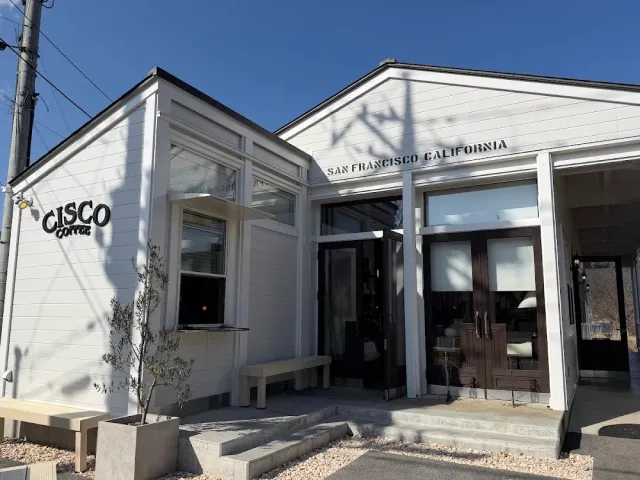 בניין לבן עם חלונות גדולים, ספסל אבן ועץ קטן בכניסה, בשמיים כחולים
